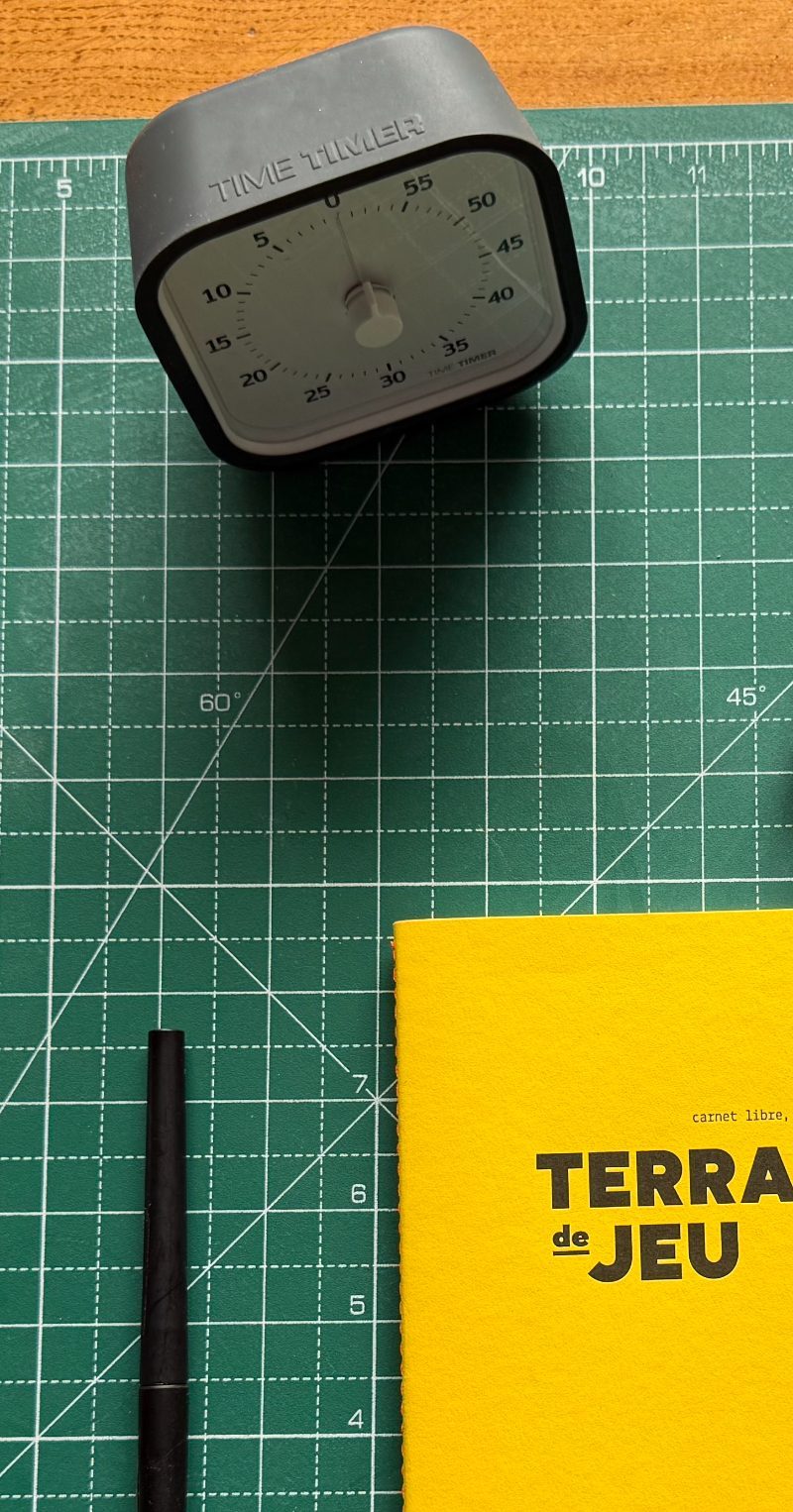 Minuteur, stylo et carnet Terrain de jeu posés sur un tapis de découpe